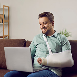 Man with arm in a sling working on a laptop. Chapter on light-duty work after injury